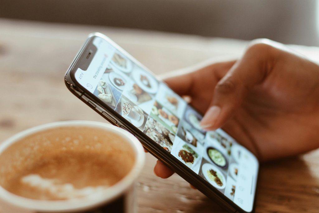 pexels photo 1542252 1542252 Hand browsing social media photos on a smartphone next to a cup of coffee indoors.